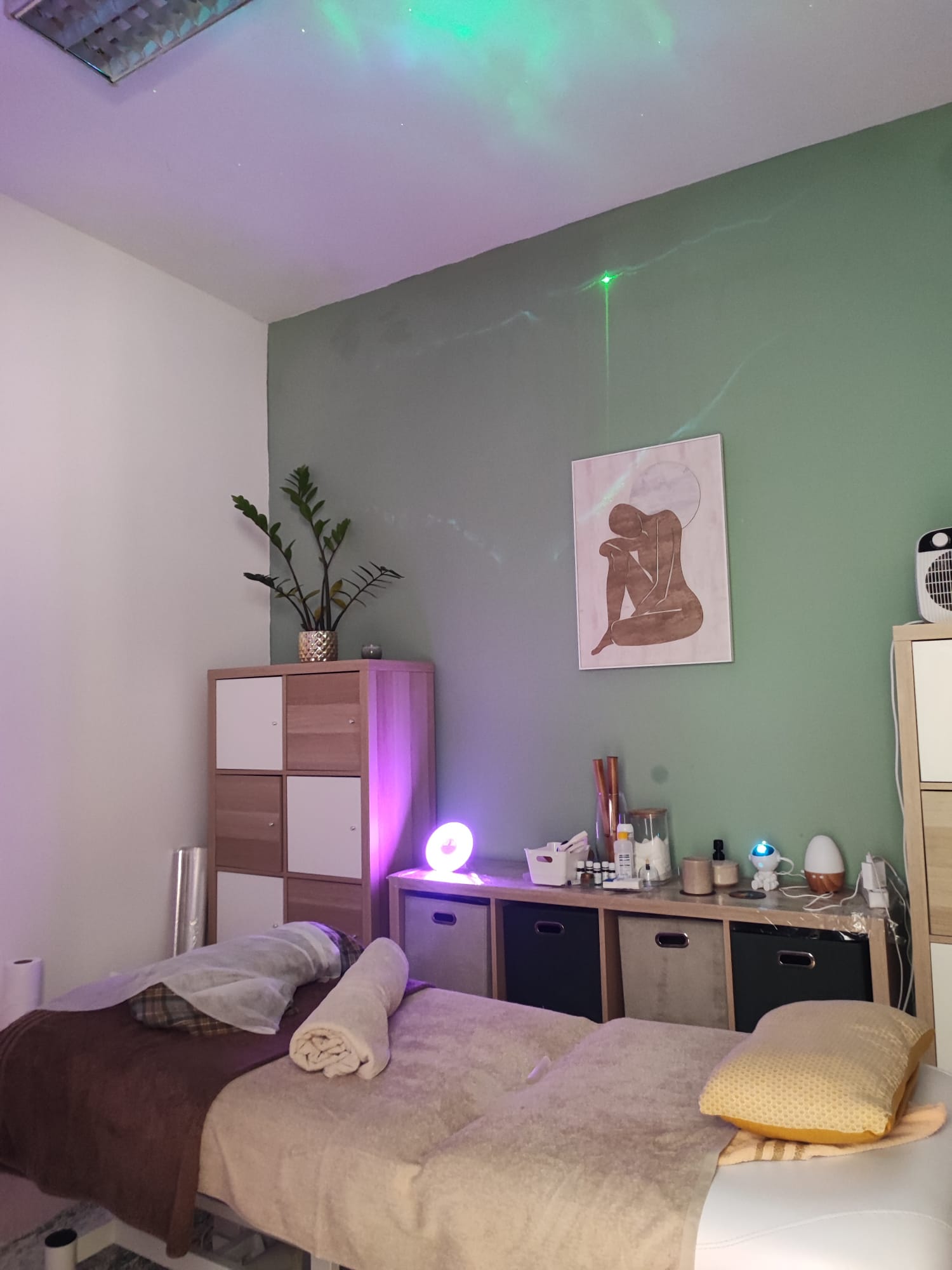 Sala de tratamento da clínica: marquesa com toalhas, parede verde e luz ambiente suave